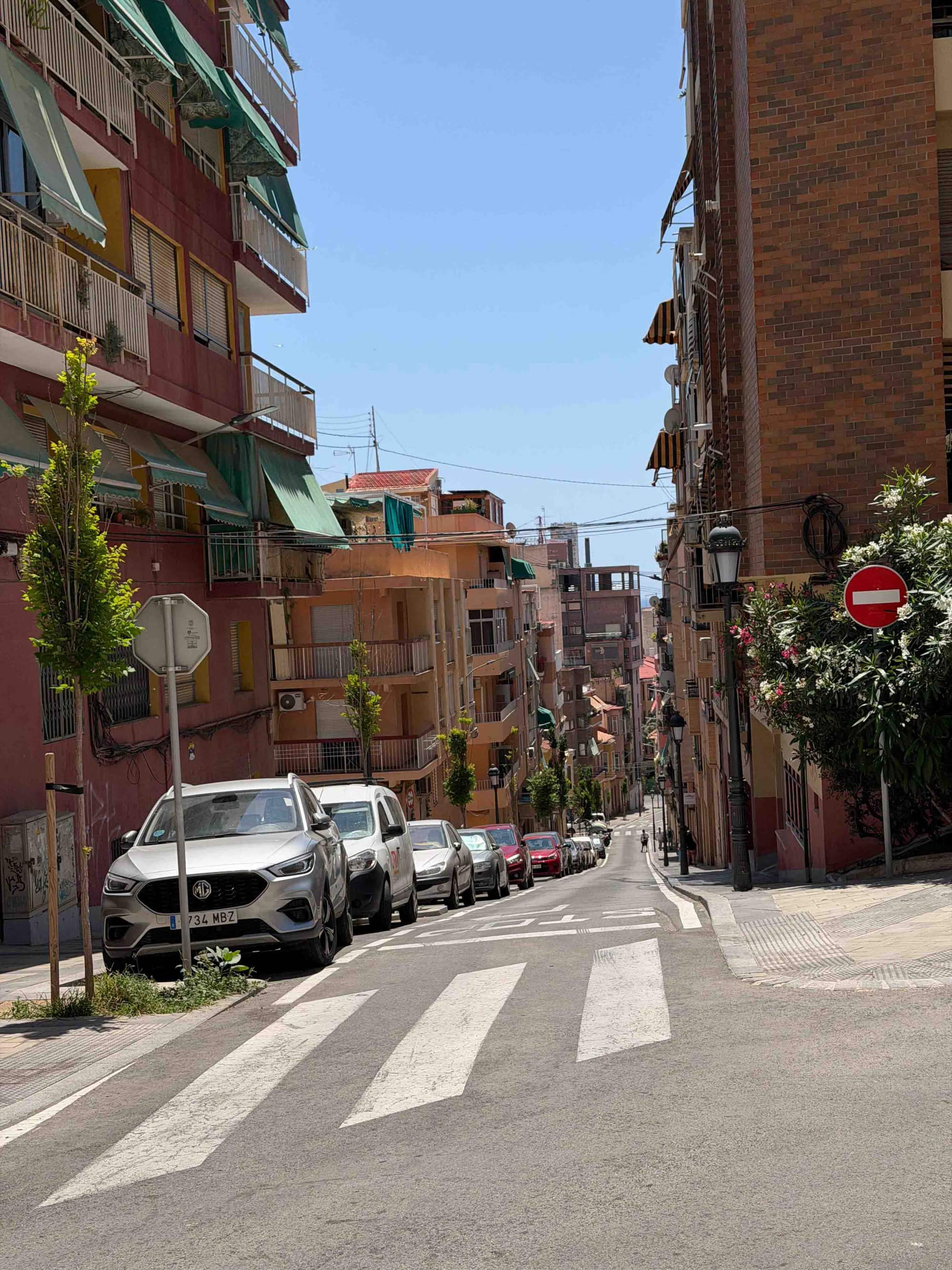 A sunny street lined with colorful buildings and parked cars.